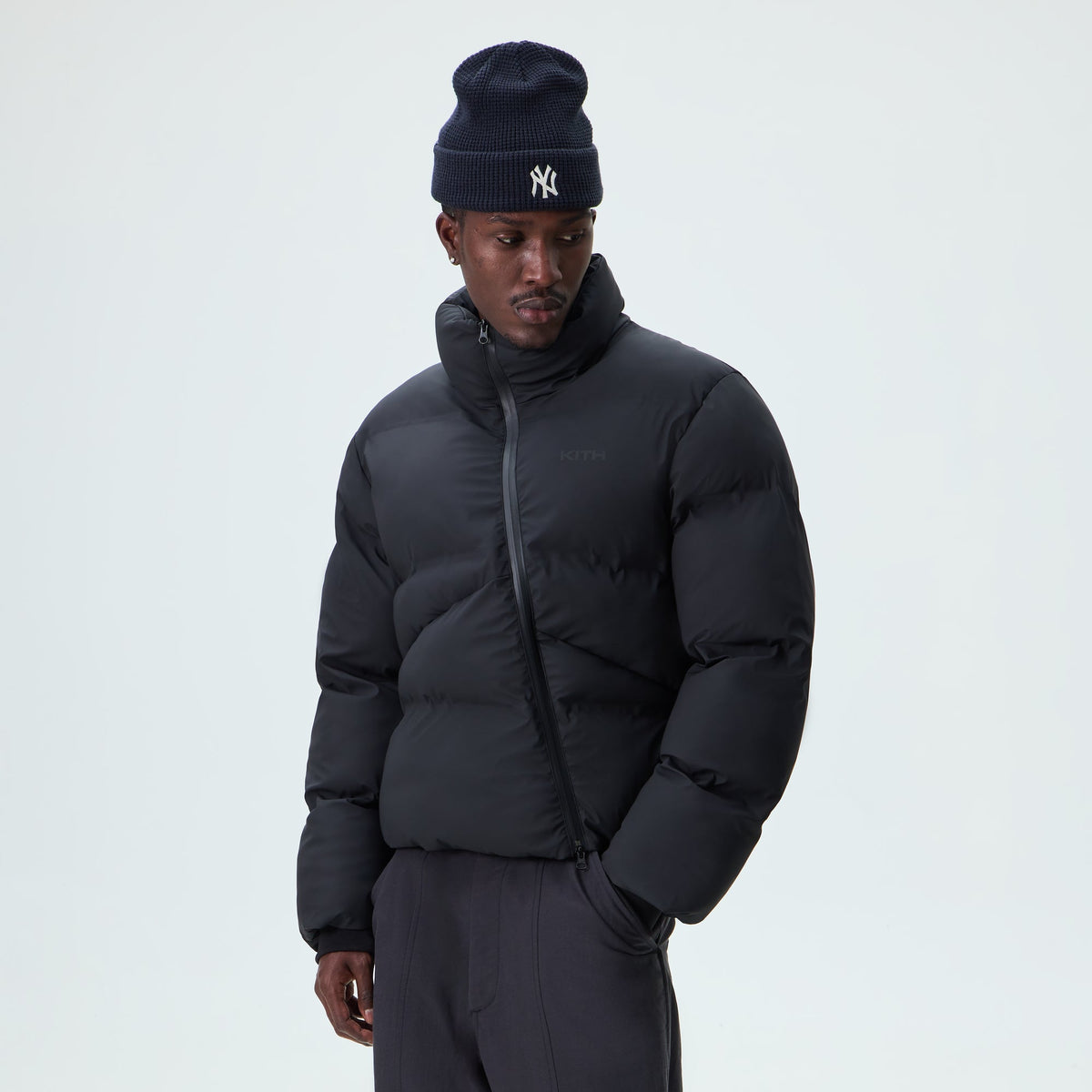 Man wearing black Kith Stretch Poly Filmore puffer with a beanie, front view