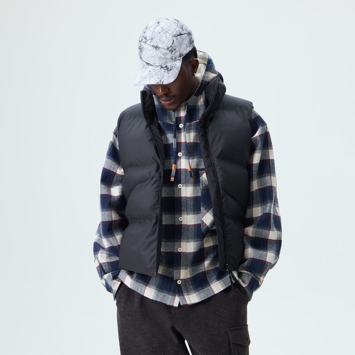 Man wearing black Kith Stretch Poly Filmore puffer vest over a plaid shirt, front view