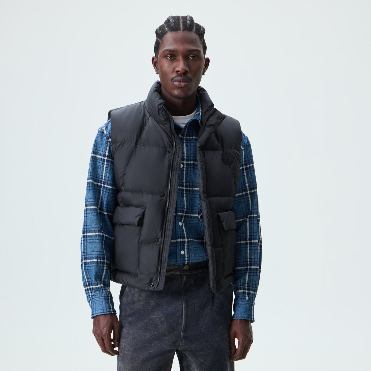 Man wearing black Kith Matte Stretch Taffeta midi puffer vest over a plaid shirt, front view