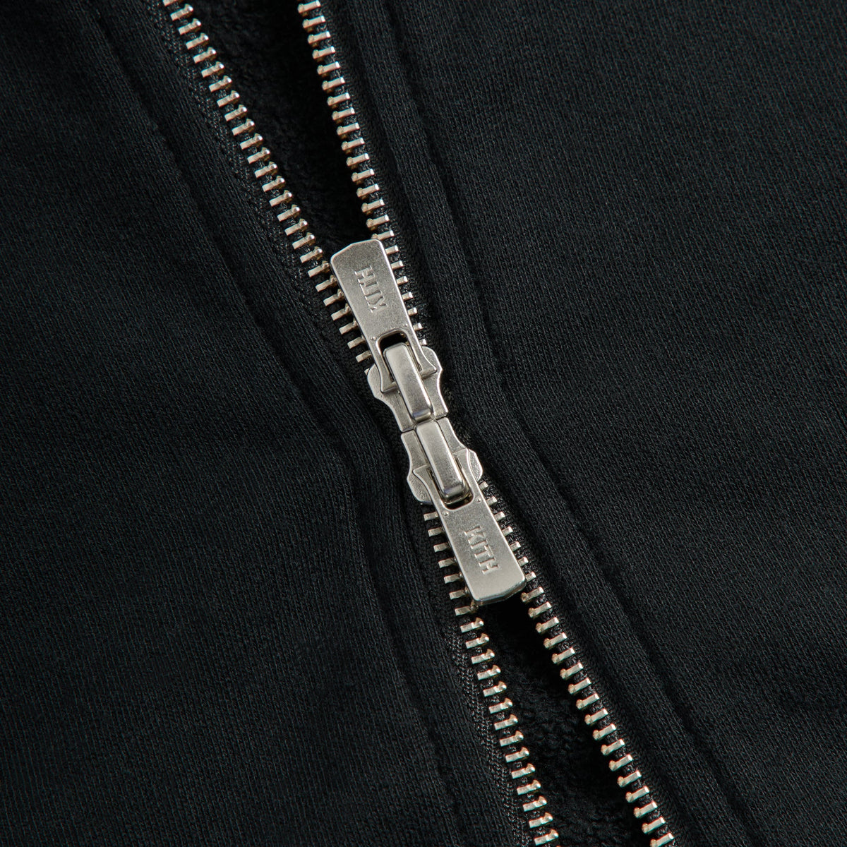 Close-up of the silver zip pull engraved Kith on the black Braxton full-zip
