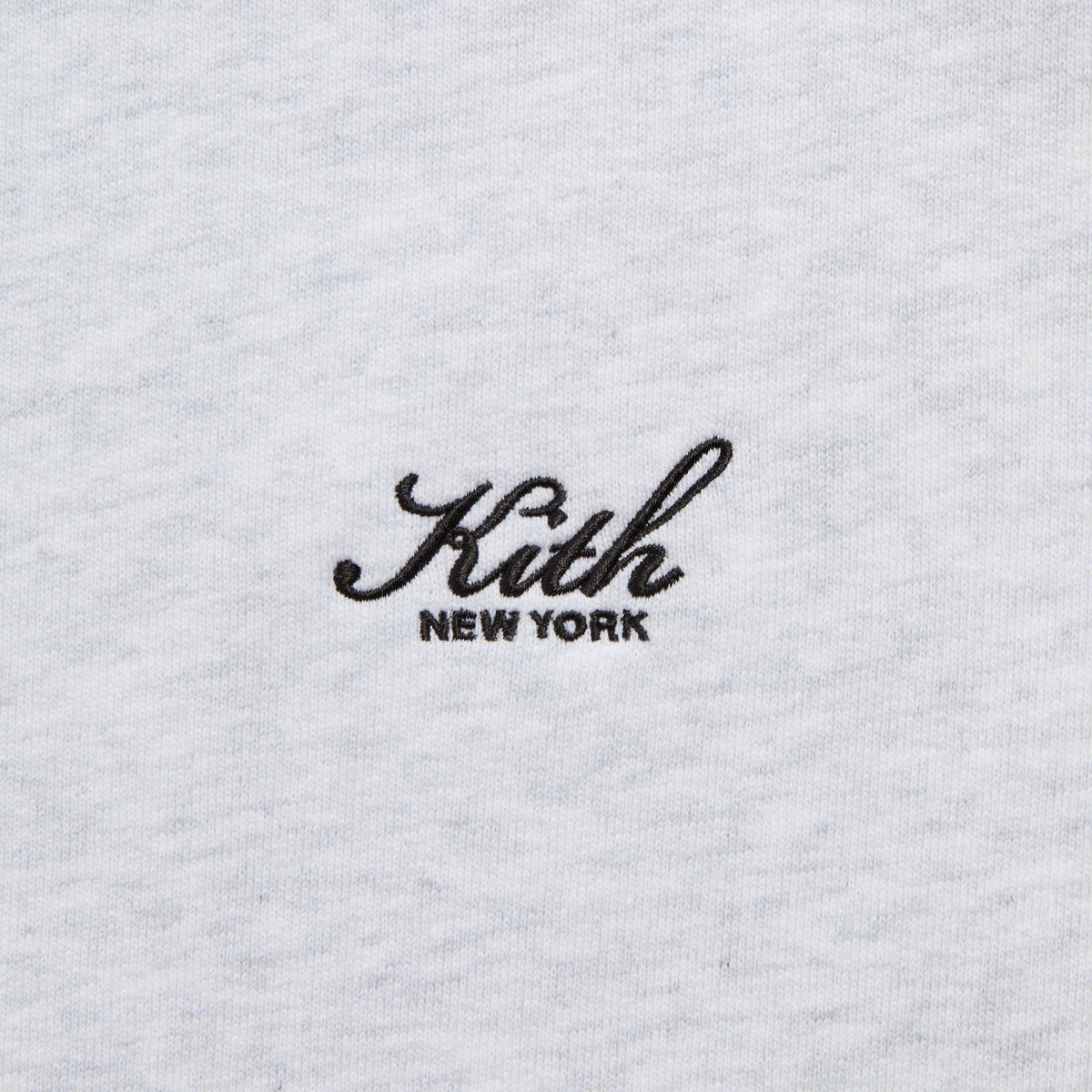 Close-up of the black 'Kith New York' script embroidery on the light grey Braxton full-zip