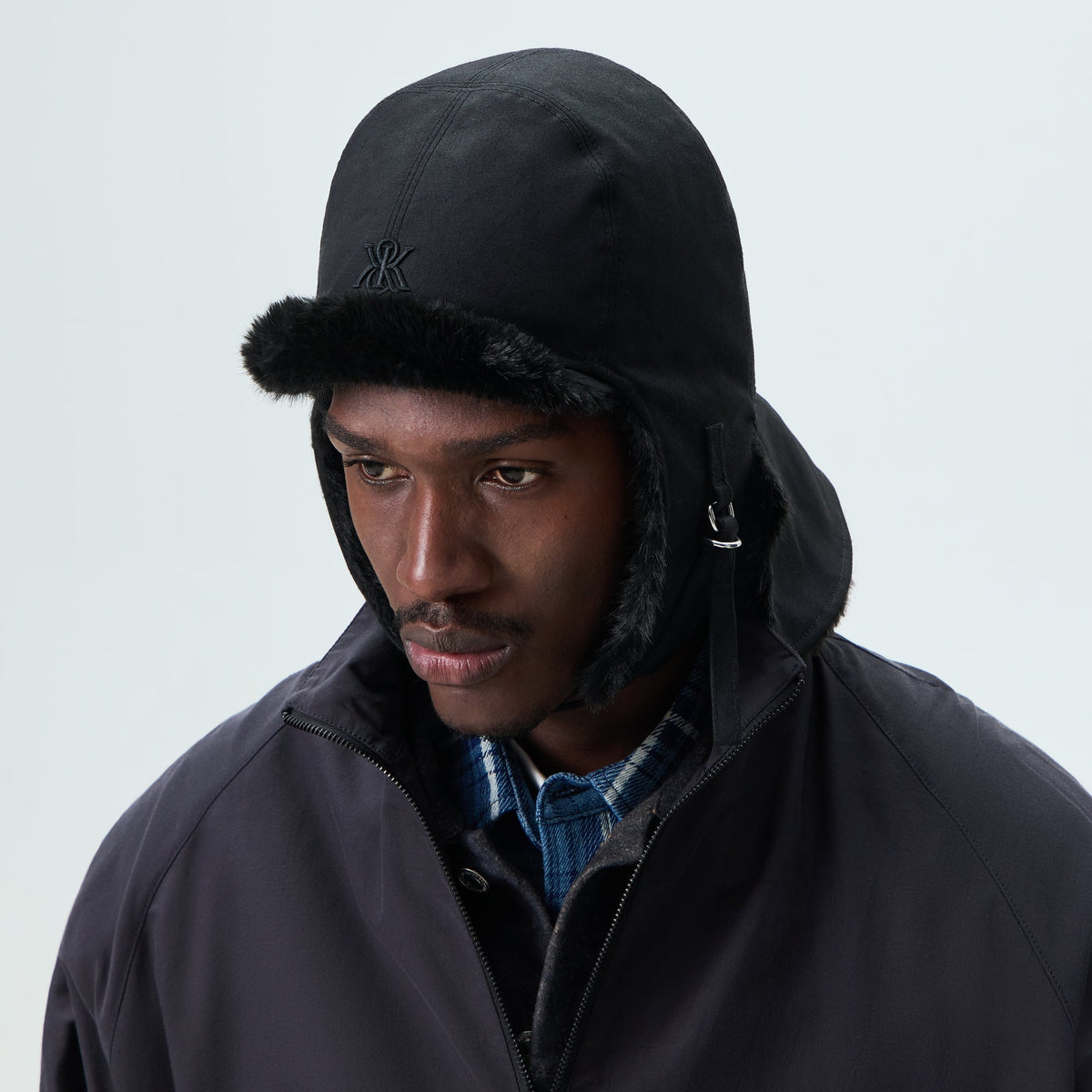 Man wearing black Kith shearling-lined waxed canvas trapper hat, front view
