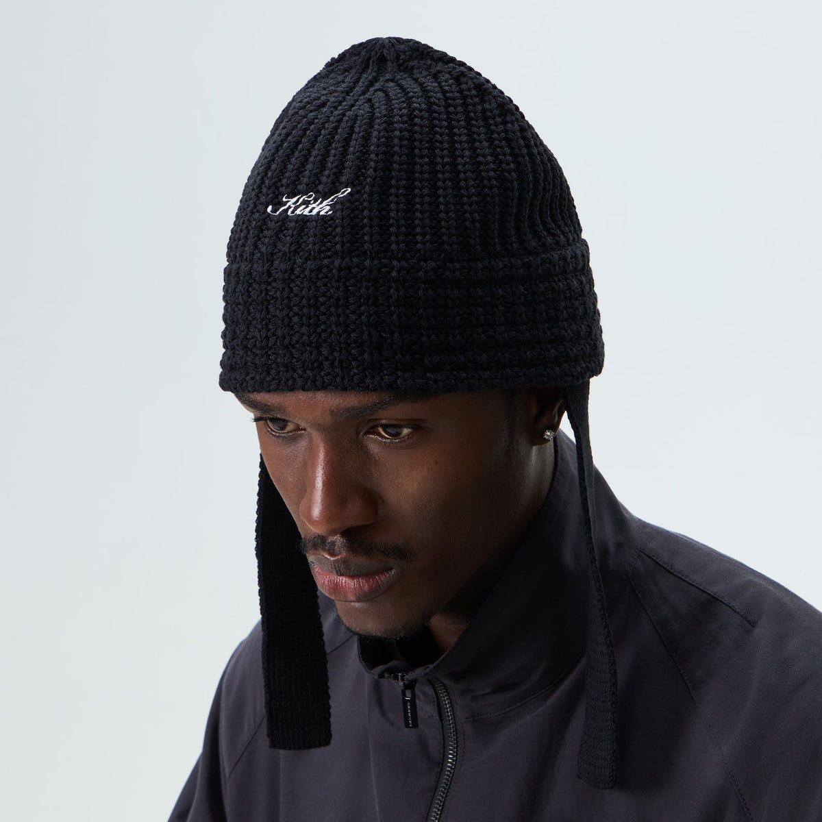 Man wearing black Kith Script knit bucket hat with chin ties, front view