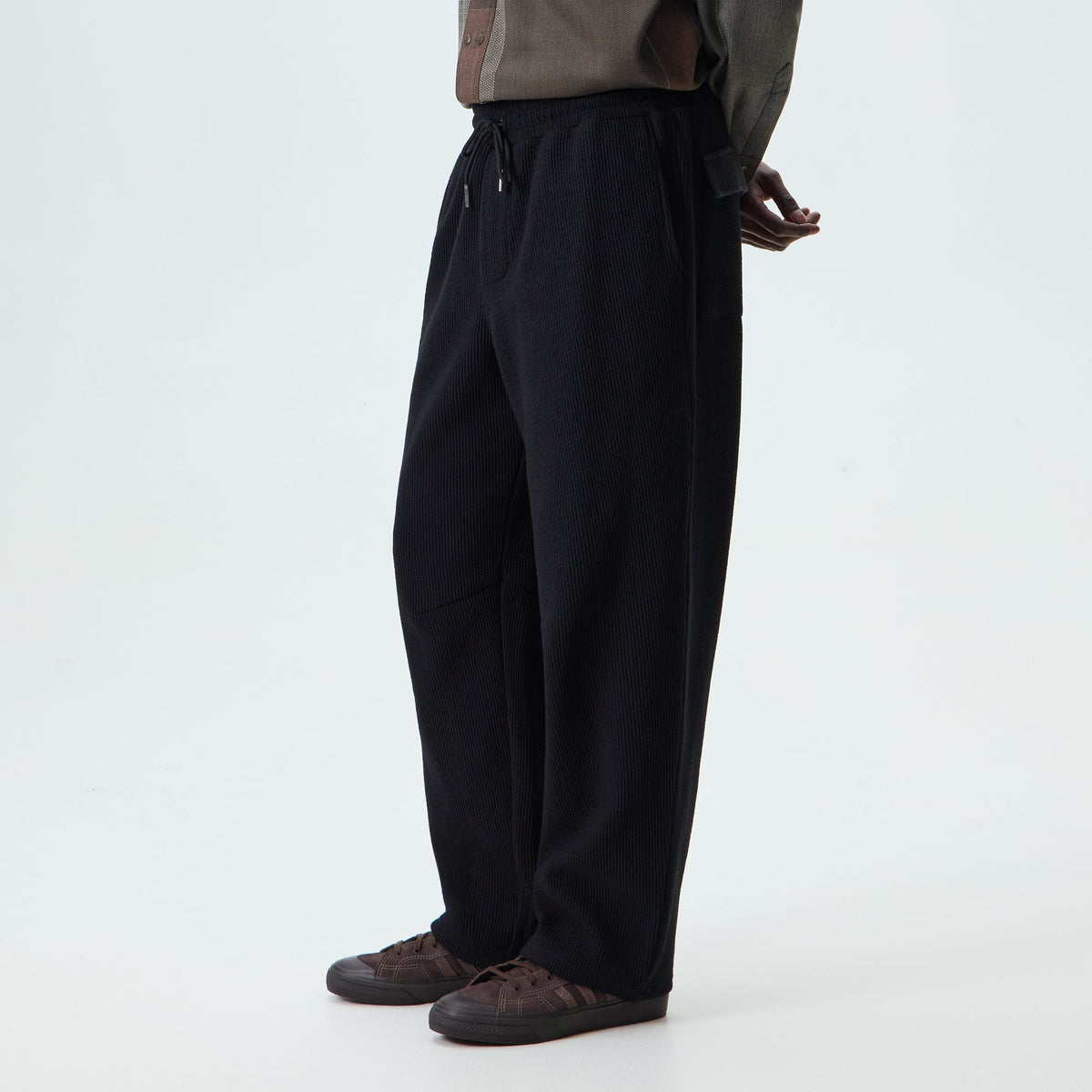 Man wearing black Kith Heavy Crepe Elmhurst trousers, side view, with sneakers
