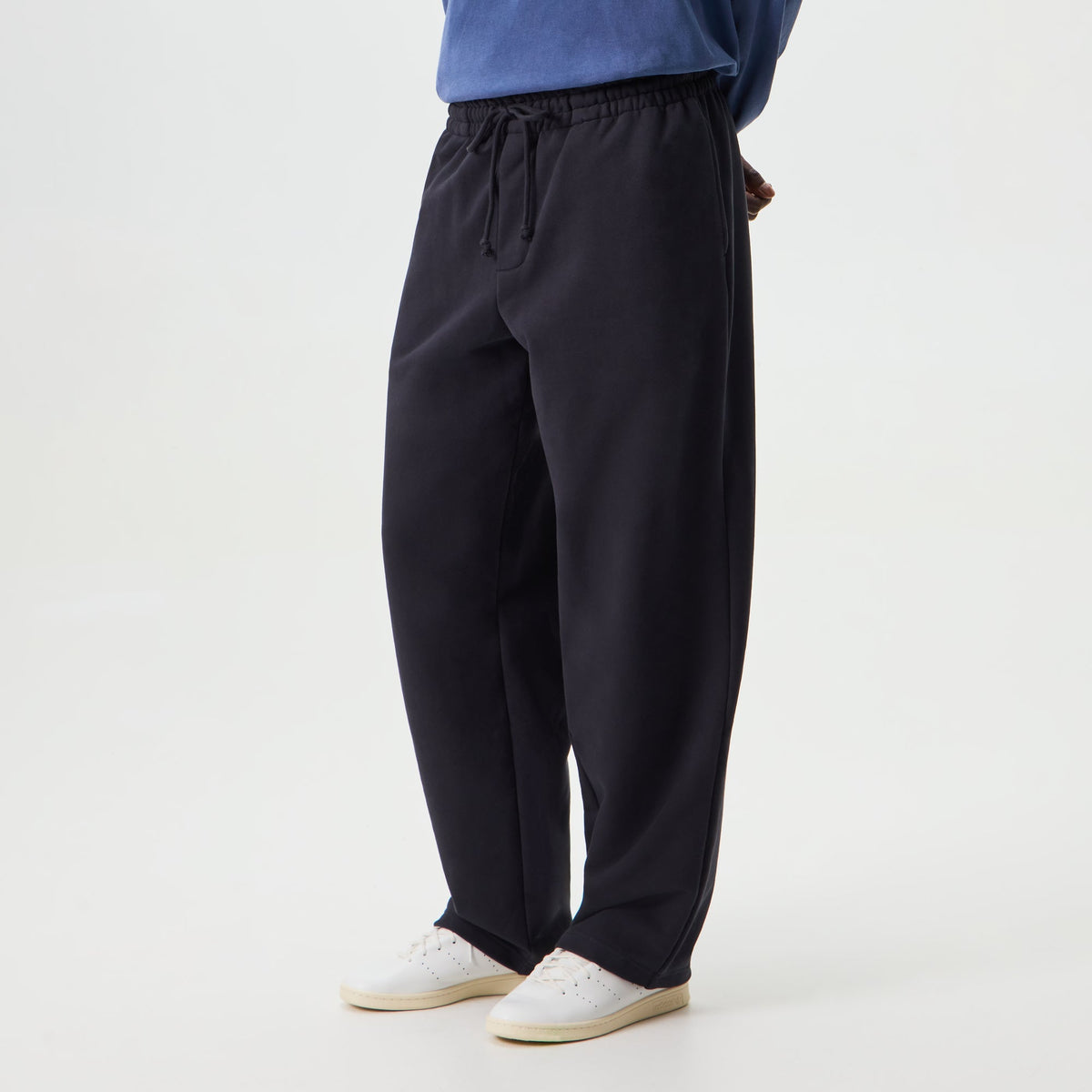 Man wearing black Kith Sueded French Terry Bryson sweatpants, side view, with white sneakers