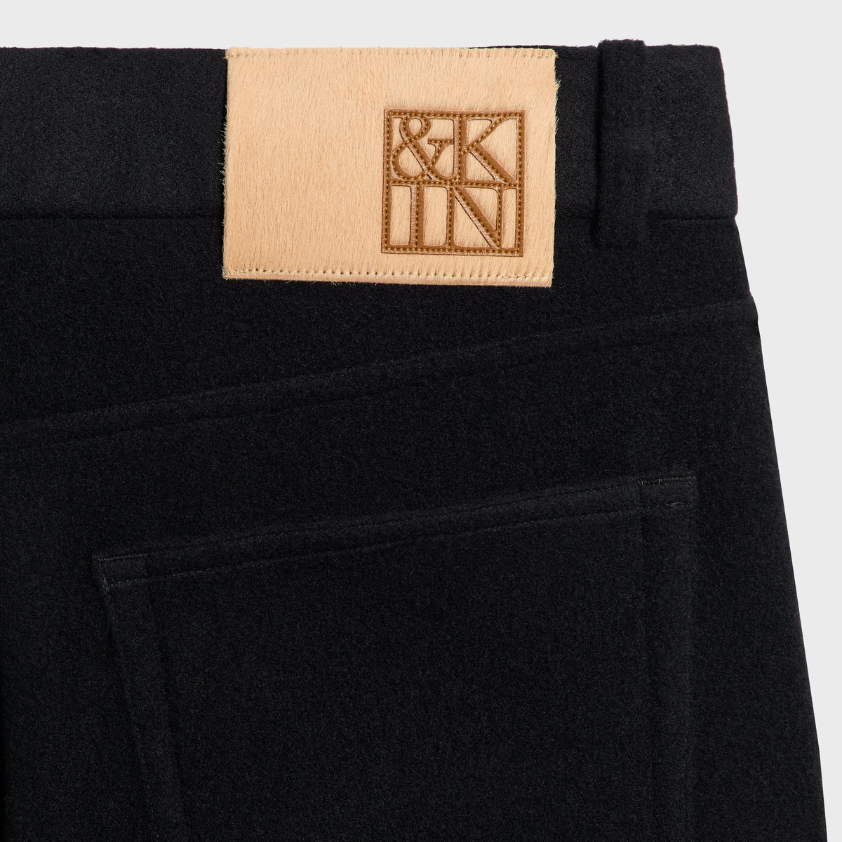 Close-up of the tan &Kin suede label on the black Wool Cashmere Brett trouser