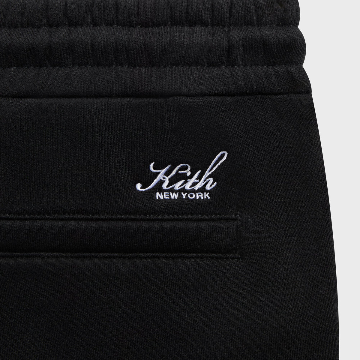 Close-up of the white 'Kith New York' script above the welt pocket on the black Bryson sweatpant